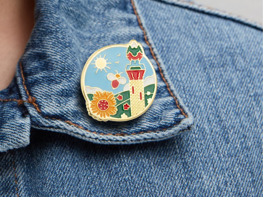 metal pin representing a sunflower, a bee and the Capricho tower by Gaudí