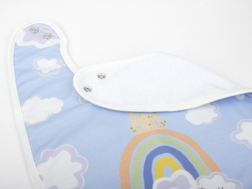 photo of a baby bib with a printed design of the Capricho de Gaudí over a rainbow in the middle of the clouds