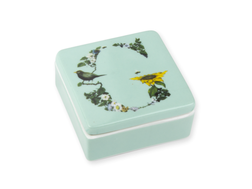 pequeña caja de cerámica de color menta con una ilustración de la inicial G impresa en la tapa